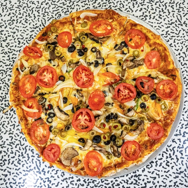 Italo pizza with tomatoes, olives, mushrooms, and onions on a patterned table.