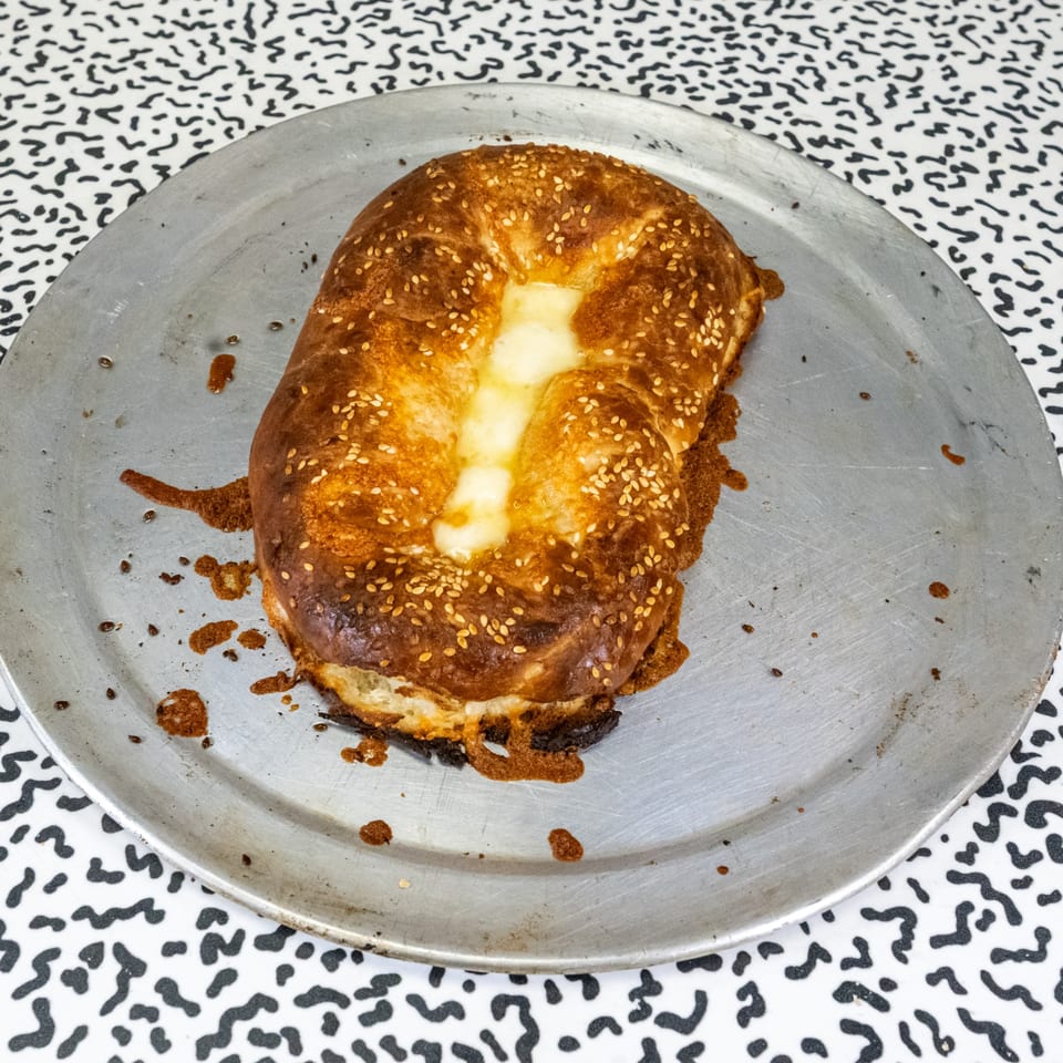 Italo pizza's golden-brown cheese bread, topped with sesame seeds, on a metal tray.