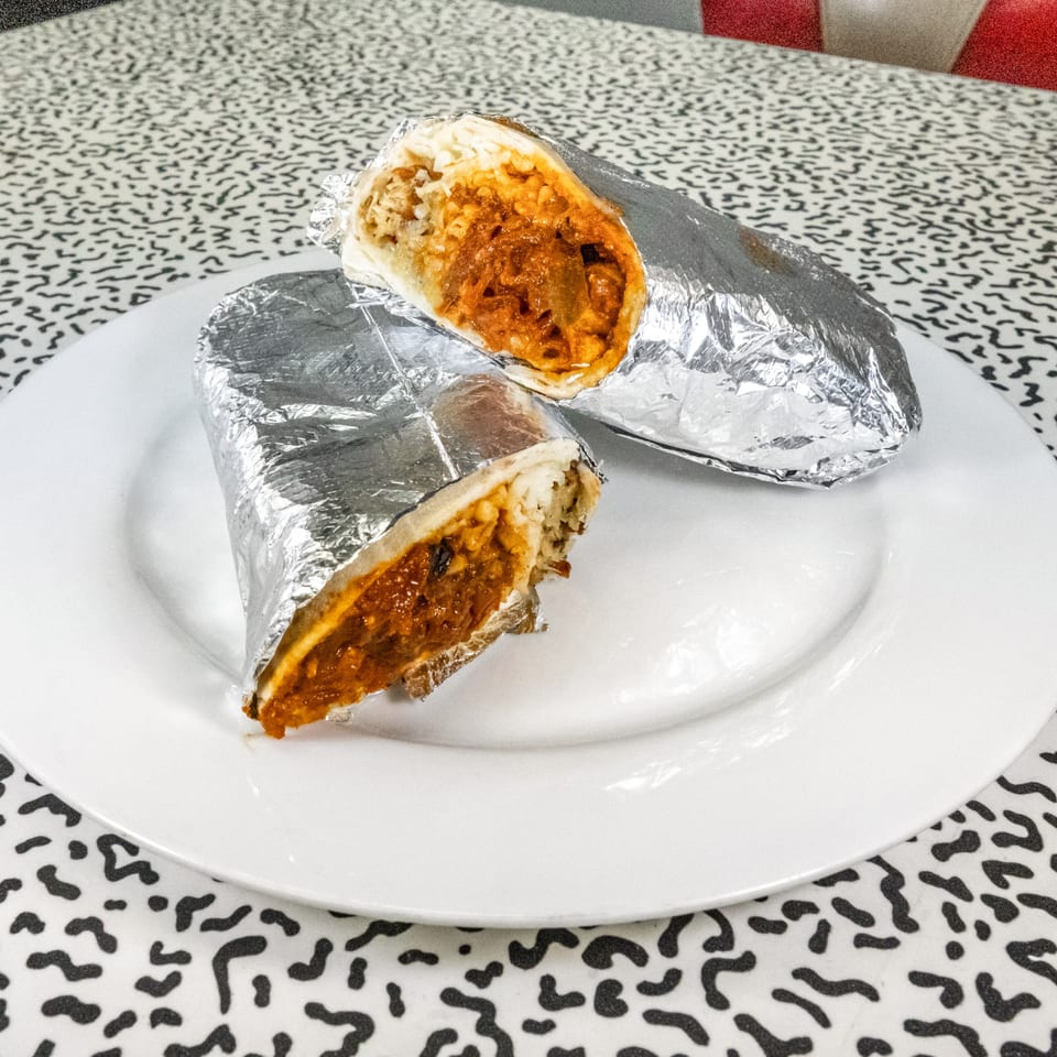 Two foil-wrapped burritos, cut open to reveal a savory filling, on a white plate.