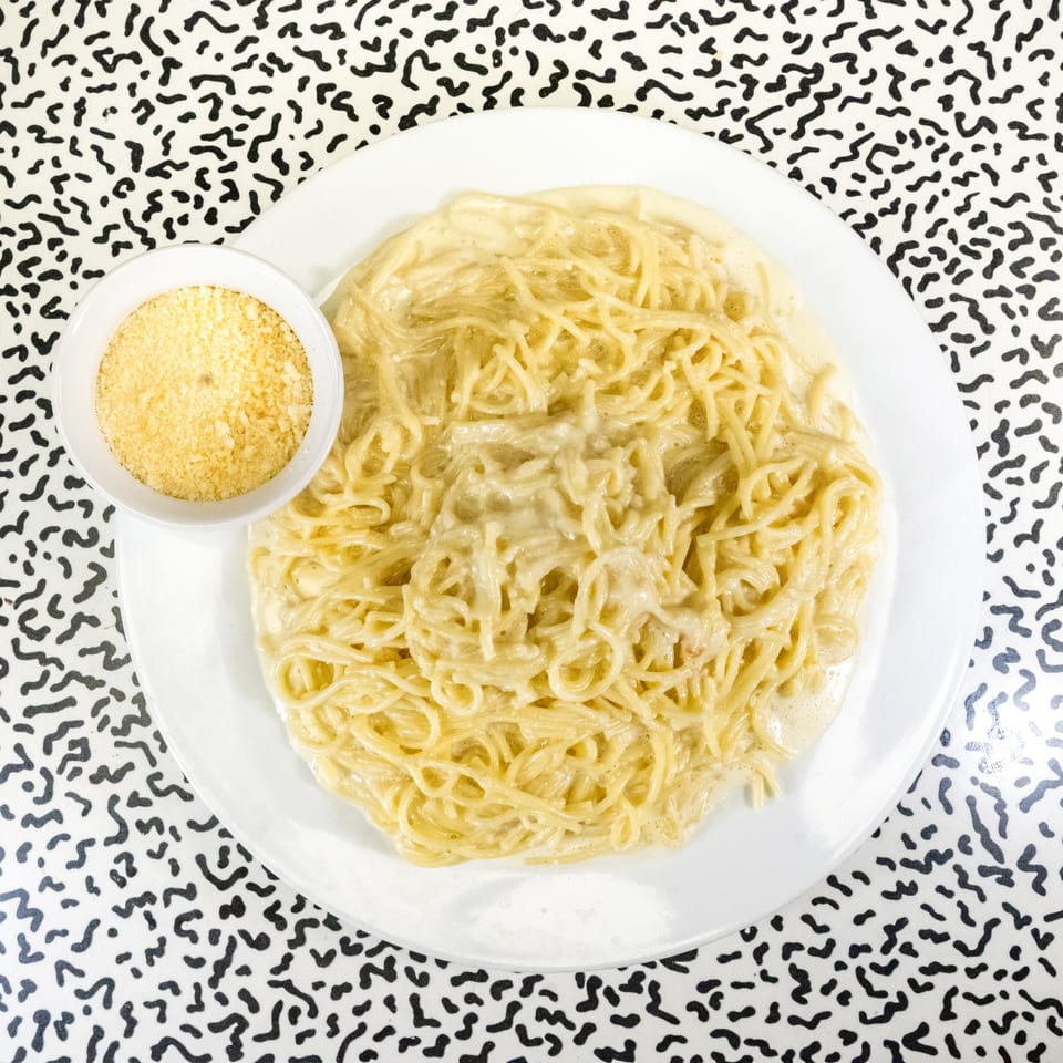Creamy spaghetti pasta with a side of grated cheese on a white plate, against a patterned tablecloth.