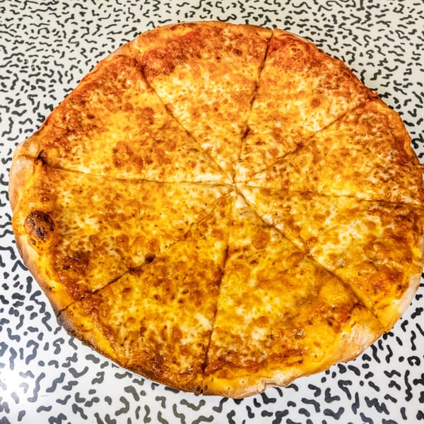 A whole Italo kosher cheese pizza, cut into slices, on a black and white patterned surface.
