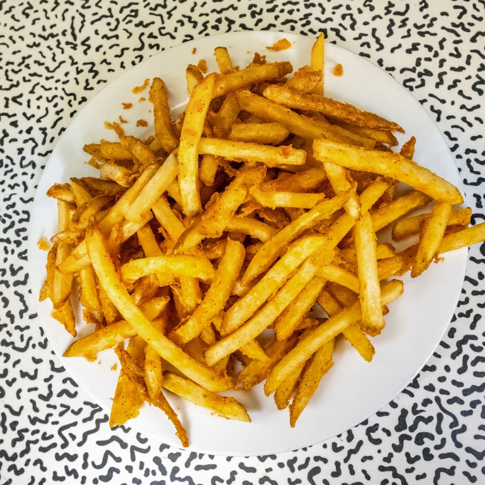 A white plate piled high with golden, seasoned french fries on a patterned table.
