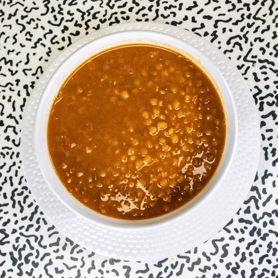 A white bowl of hearty, orange-brown lentil soup sits on a black and white patterned tablecloth.