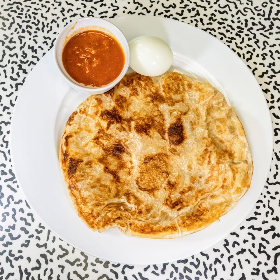 A golden-brown flatbread, a white bowl of red sauce, and a boiled egg on a white plate.