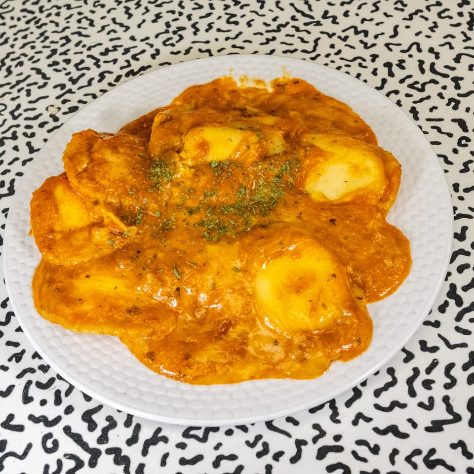 Italo pizza's ravioli pasta in a rich orange sauce, garnished with green herbs on a white plate.