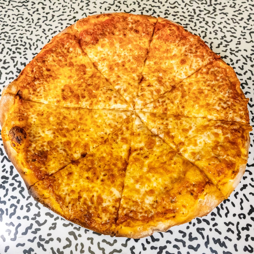 A whole, sliced cheese pizza with a golden-brown crust sits on a patterned white and black table.